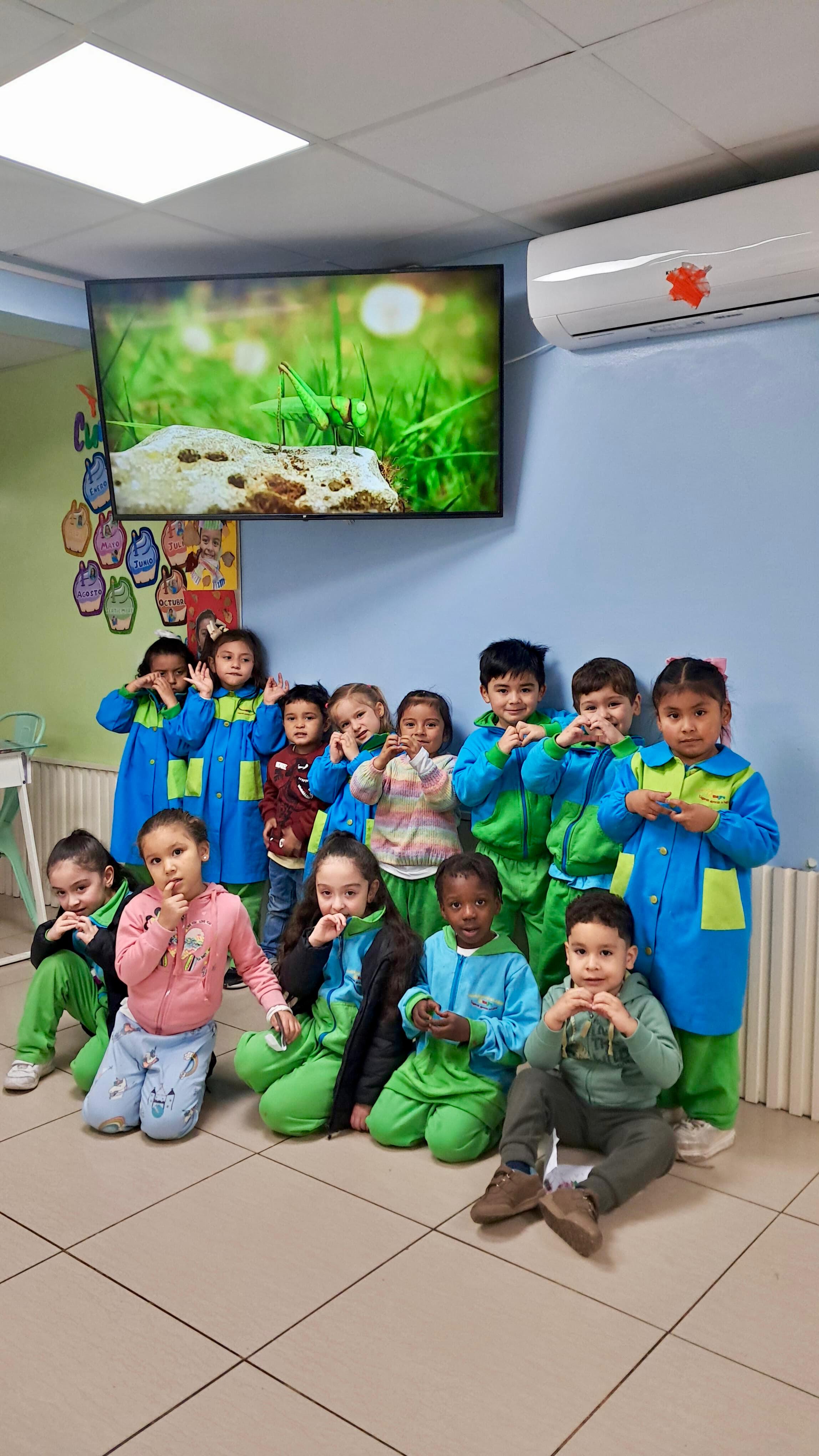 Grupo de niños haciendo señas de corazón frente a una pantalla con un insecto